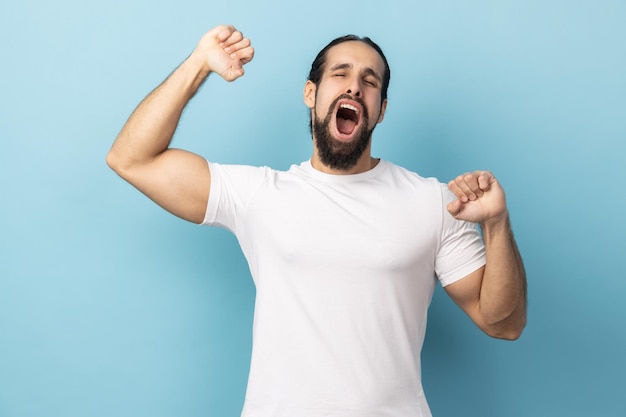 Man standing and yawning with closed eyes and raised arms waking up early