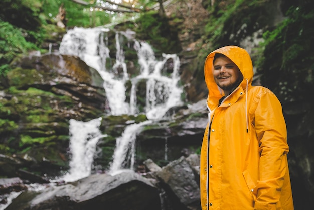 Man standing in yellow raincoat and looking at waterfall