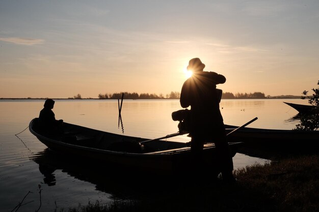 A man stands on a boat in front of a sunset.