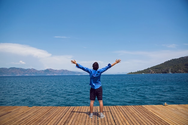 man stands by the sea on the pier in a blue shirt in sneakers