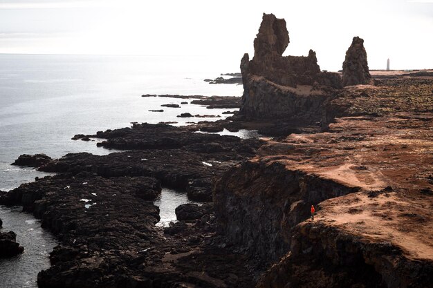 A man stands on a cliff with a red shirt on.