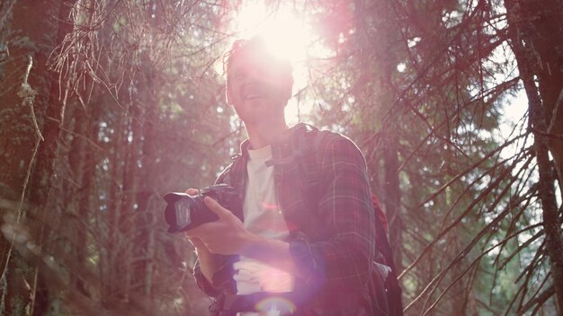 Foto un uomo si trova in una foresta con una macchina fotografica sulla schiena.