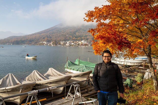 A man stands in front of a lake with a mountain in the background.