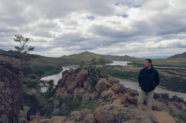 A man stands high on a hill and looks into the distance Below is the river and the mountains