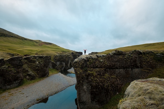 Un uomo si trova su una collina con le mani alzate. paesaggio islandese.