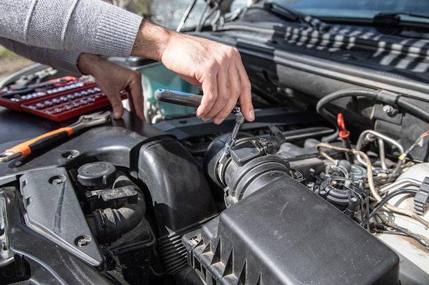 A man stands at the open hood of a car with tools