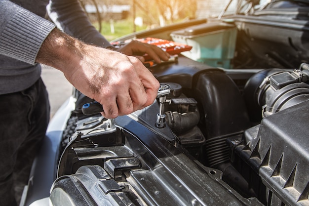 A man stands at the open hood of a car with tools