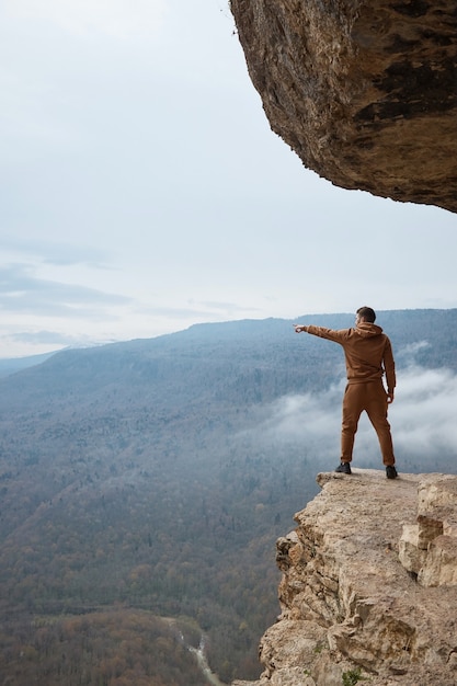 A man stands on a rock and points his finger at the valley, the mountains, the view of the forest from the cliff