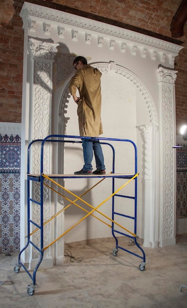 A man stands on a scaffolding that has a blue and yellow scaffolding. wall painting, arches.