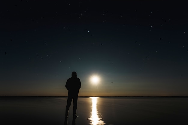 男は星空の下で月の夕日に立っています