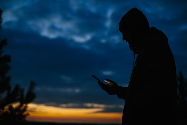 Мужчина стоит с телефоном на фоне ночного неба Путешественник в горах на закате