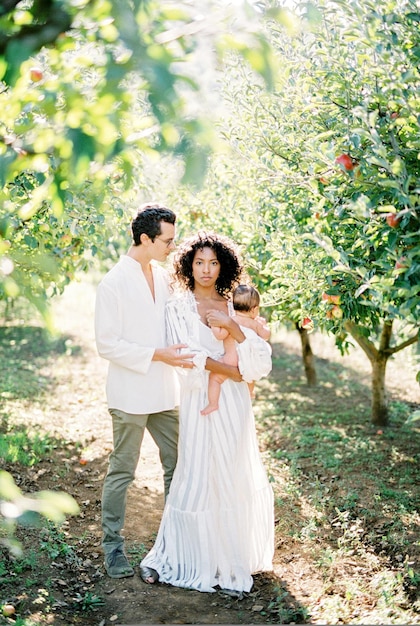 Man stands next to a woman with a baby in her arms in an apple orchard