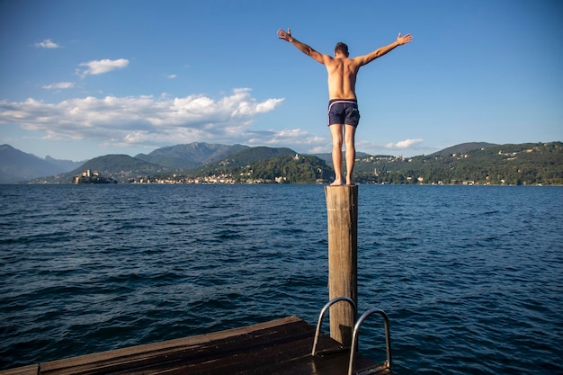 A man stands on a wooden post on a lake shore
