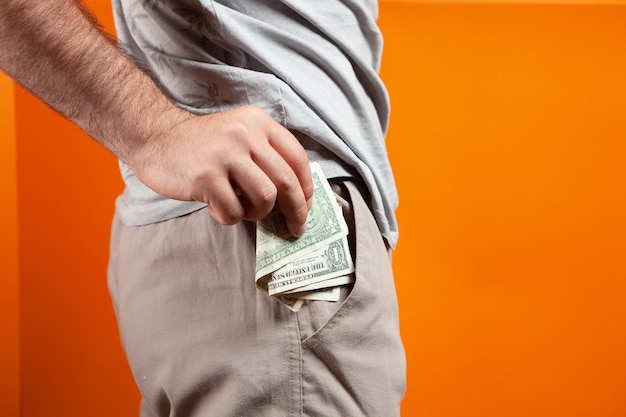 Man steekt geld in zijn zak op oranje achtergrond