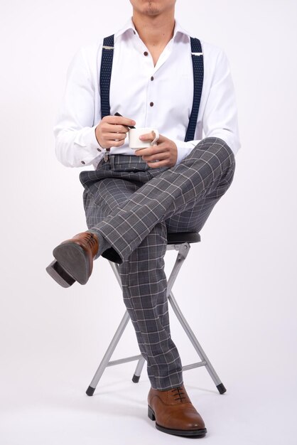 man stirring a cup of coffee sitted on a chair with a white background