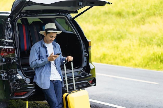 Photo man stood in the car with his mobile phone and luggage