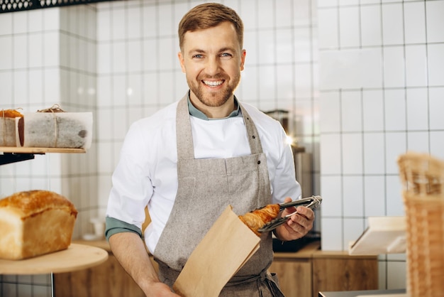 Man stopt croissant in een papieren zak met een tang