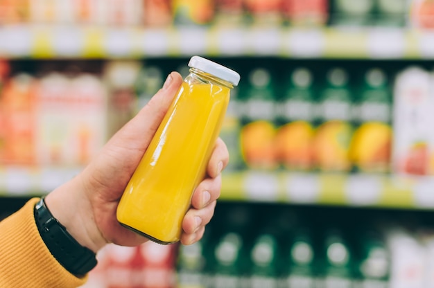 Foto l'uomo in un negozio tiene in mano una lattina di succo d'arancia sullo sfondo di un rack.