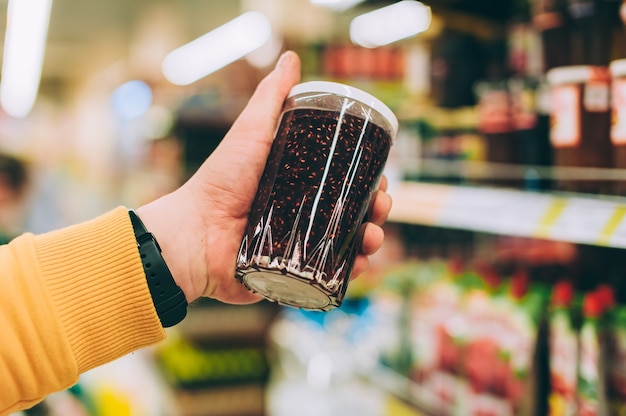 Man in a store holds a jar of jam in his hand, against the backdrop of a rack.