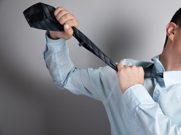 Man strangles himself with his tie on gray surface