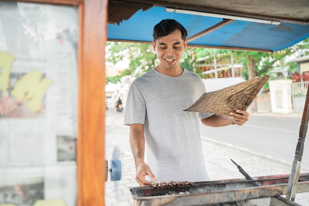 Man street food seller of chicken satay with food cart selling sate ayam