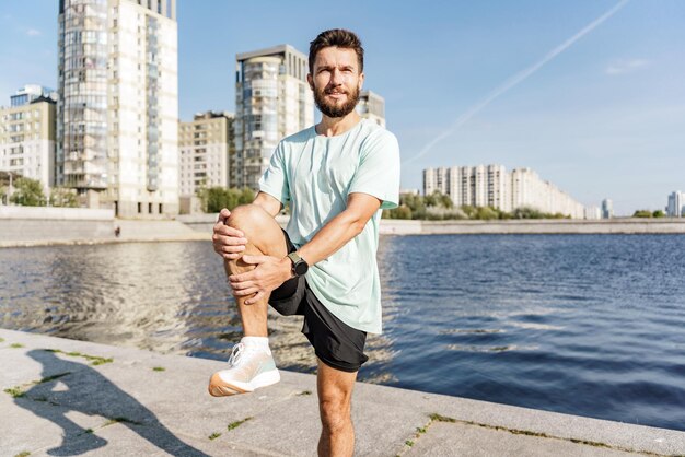 A man stretches by a city riverbank highrise buildings reflecting the days bright light