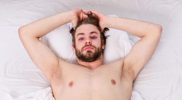Мужчина потягивается в постели Изображение, на котором молодой человек потягивается в постели Мужчина расслабляется в постели