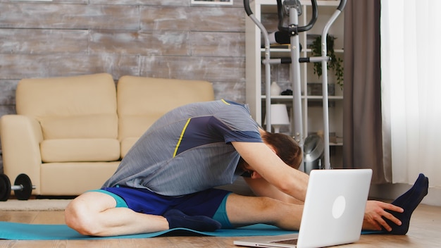 Man stretching his body on yoga mat during online fitness class.