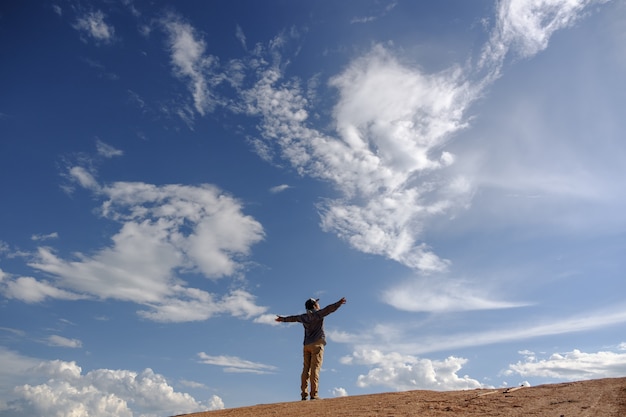 Photo man stretching out his arms on grounds.asian men wear gray shirts, brown pants are standing outdoors.look at the copy space.wear a hat and scarf.man standing on the ground.