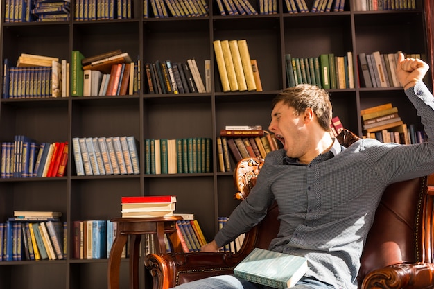 Man stretching and yawning as he wakes up from a nap in a comfortable armchair in a library