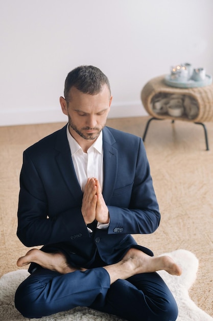 A man in a strict suit does Yoga while sitting in a fitness room