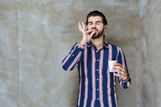 Man in striped shirt holding a white disposable cup of drink and enjoying the taste