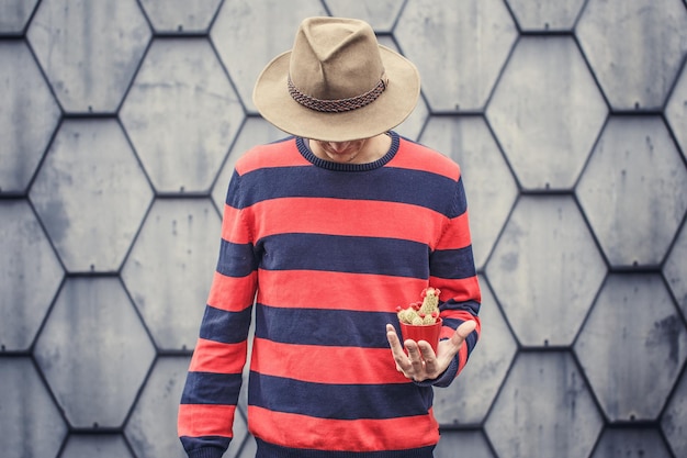 Photo man in stripes sweater holding small cactus.