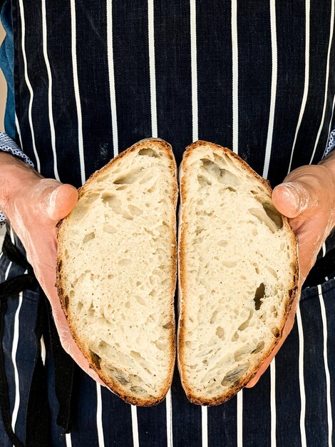 Foto uomo con un grembiule blu spogliato che tiene un pane di lievito al forno un pane tradizionale francese tagliato a metà