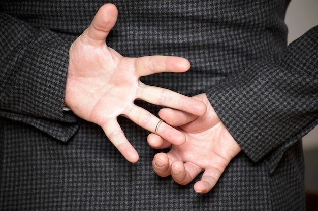 A man in struggling to remove wedding ring from his finger holding hands behind his back