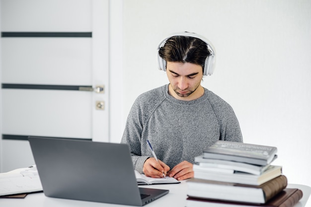 Man student met koptelefoon op hoofd schrijven in notitieblok werken op computer