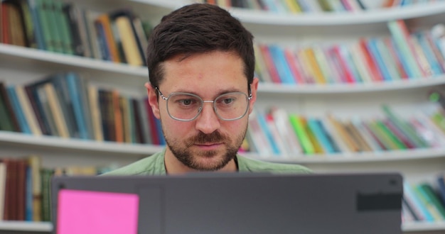 Studente uomo che prepara esami e lezioni di apprendimento in biblioteca che fa ricerche su laptop e naviga in internet concetto di autoeducazione