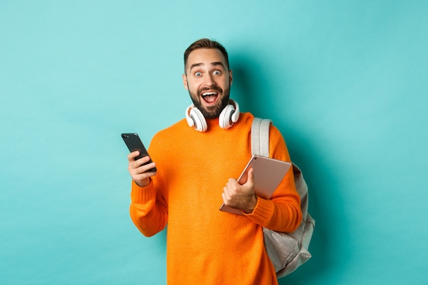  man student with headphones and backpack, holding digital tablet and smartphone, looking