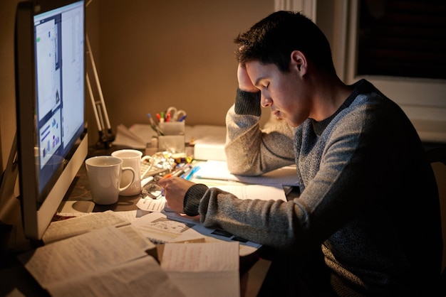 Man studying and tired in night by computer for test assessment or stress in college dorm room Male university student education and burnout with fear fatigue and anxiety with books for learning