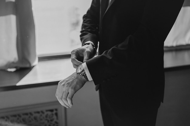 Man in a stylish black suit with a watch on his wrist straightens his suit