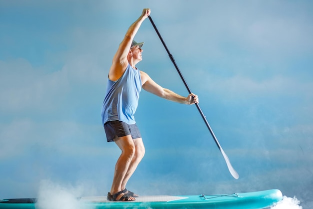 A man on a sub board with an oar rows in the fog against the background of clouds