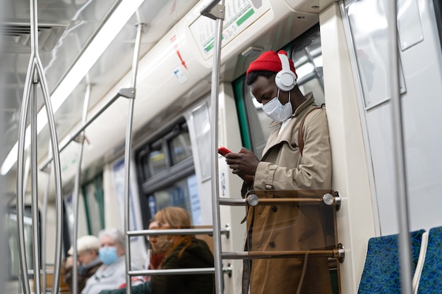 地下鉄の電車の男が携帯電話を使ってフェイスマスクを着用