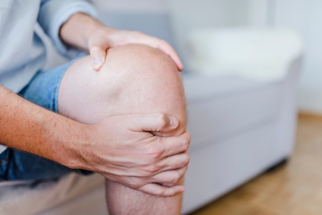 Man suffering from knee pain sitting sofa