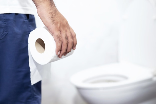 Foto l'uomo soffre di diarrea e tiene un rotolo di carta igienica davanti allo stomaco della vasca igienica