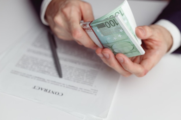 Man in suit counts wad of money before signing contract close up of hands with money