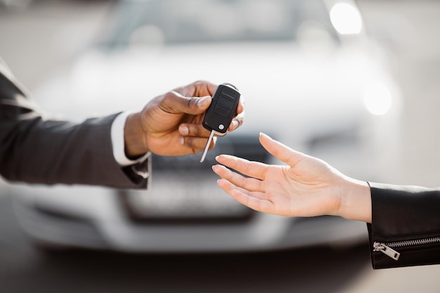 A man in a suit extends his hand to a woman in a leather jacket holding a car key the woman reaches