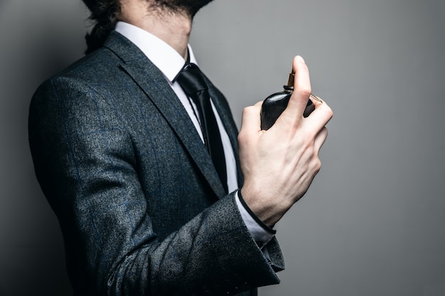 Man in a suit and glasses sprinkles with perfume on a gray wall