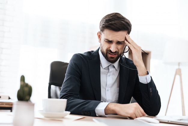 A man in suit has a headache. He keeps his hands.