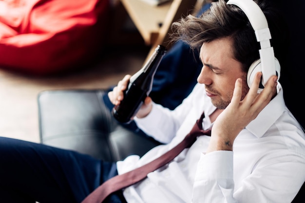 Photo man in suit holding bottle and listening music in headphones