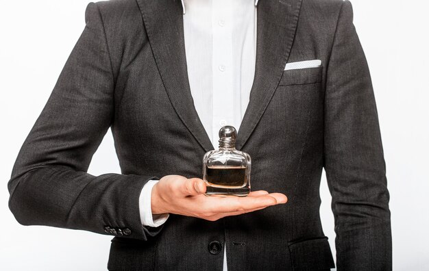 Man in a suit holding a bottle of perfume isolated on white